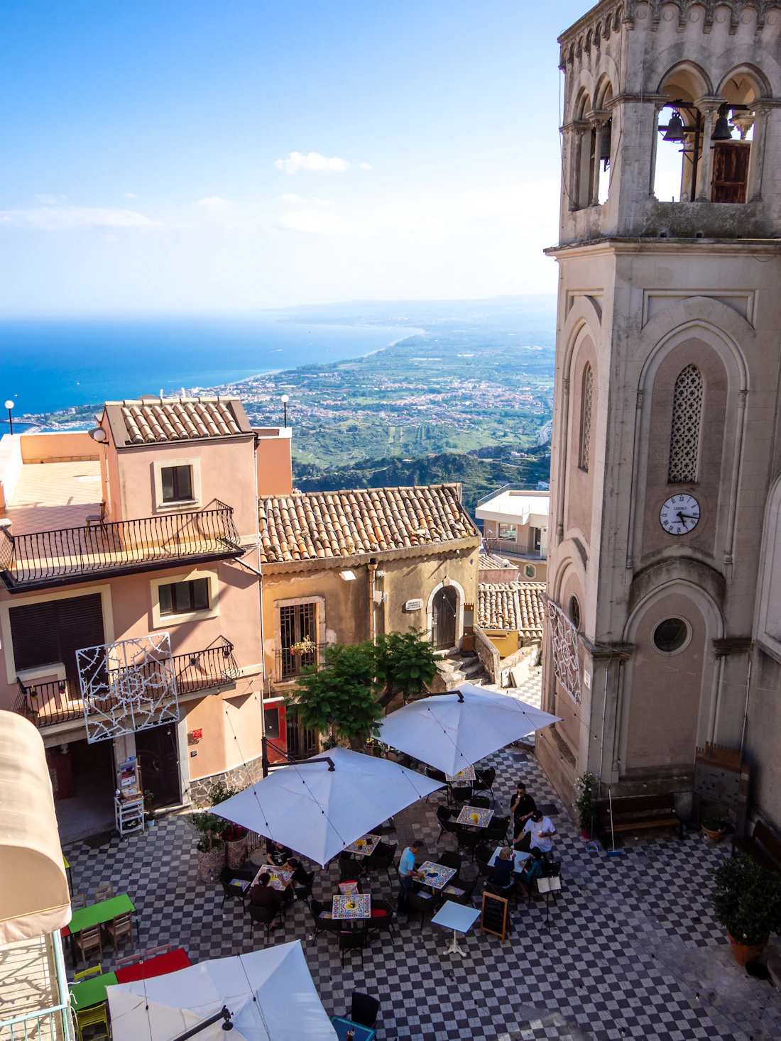 A Sicilian street with a baroque bell tower and the coast beyond
